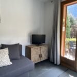 Knusse woonkamer met bank, tv en grote raam met uitzicht op tuin.