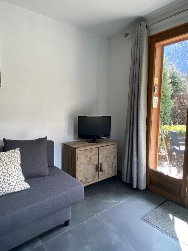 Knusse woonkamer met bank, tv en grote raam met uitzicht op tuin.